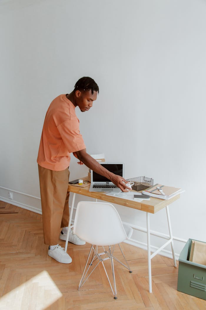 hero-02 A man standing at a desk organizing papers and electronic devices in a modern office setting.