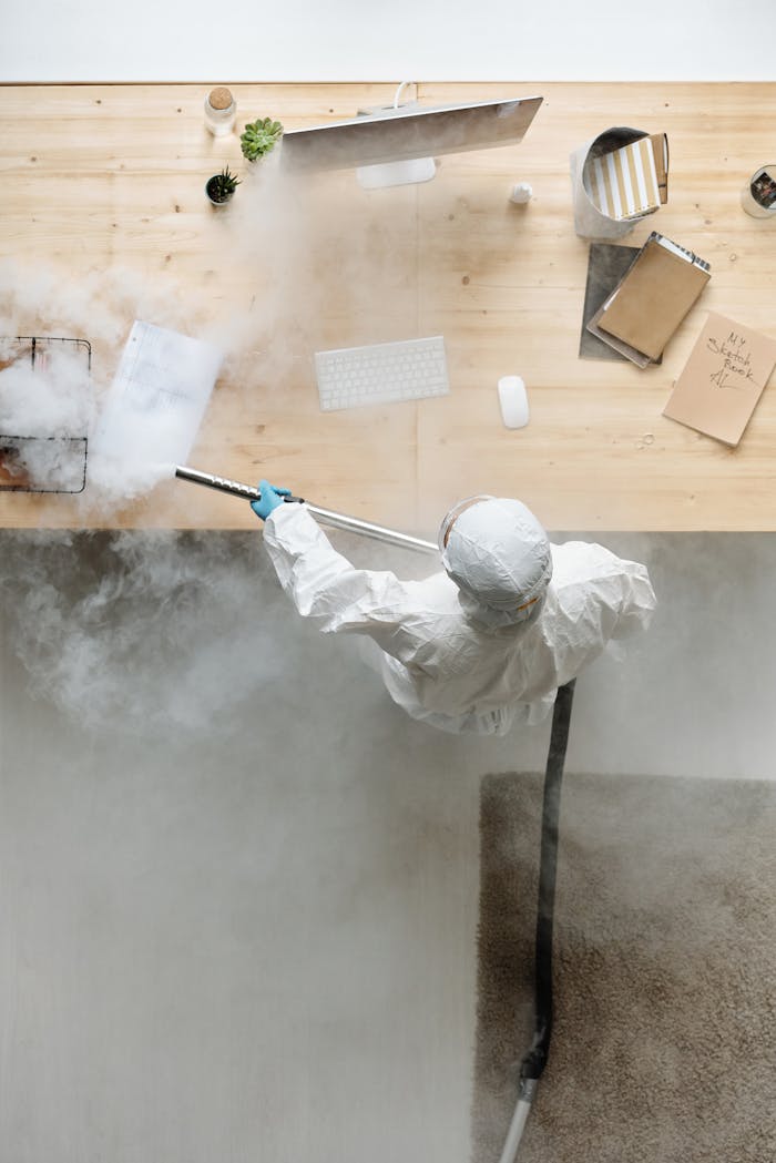 services-02 A person in PPE disinfects an office desk with steam, ensuring cleanliness and safety.